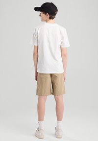 T-shirt bianco in cotone, pantaloni corti beige, cappellino nero, sneaker bianche. Design semplice, maniche corte, texture liscia, vestibilità casual.