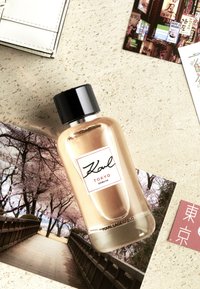 Bouteille de parfum Karl Lagerfeld Tokyo avec un design en verre clair et incurvé. Capuchon noir, étiquette blanche avec bord rouge et texte minimaliste.