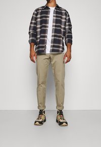 Koszula flanelowa w kratę w kolorze granatowym z białymi i czerwonymi akcentami, biała koszulka, beżowe spodnie z podwiniętymi mankietami oraz beżowo-czarne sneakersy.