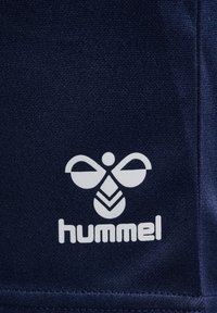 Mörkblått tyg med en texturerad yta har en vit logotyp av en bi och ordet "hummel", placerad i nedersta vänstra hörnet.