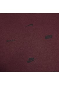 Maroon fabric featuring black Nike logos and text, smooth texture, evenly distributed branding, and a simple, minimalist design.