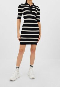 Robe polo à manches courtes rayée noir et blanc avec une texture côtelée et des boutons au niveau du col ; associée à des baskets blanches à semelles épaisses.
