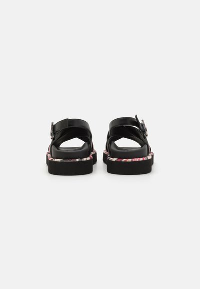 Sandales noires avec une semelle plate, une sangle ajustable et une bordure en tissu à motif autour du bord. Matériau supérieur lisse et quincaillerie minimale.