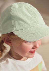 Cappellino da baseball in cotone verde menta con visiera curva, design strutturato e dettagli di cuciture, indossato da un bambino con capelli biondo chiaro.