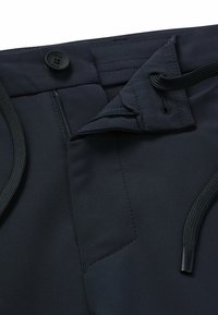 Mörkblå byxor med knappstängning, dragkedjeficka och snörning. Tillverkade av ett slätt, hållbart tyg med rena sömnadsdetaljer.