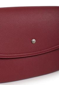 Pochette en cuir rouge avec une surface texturée, présentant une forme arrondie, un fermoir à pression en argent proéminent et un détail de bord cousu.