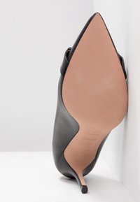 Czarny skórzany but na wysokim obcasie z noskiem w szpic i cienkim obcasem typu szpilka. Gładka faktura, jasnobrązowa podeszwa i smukła sylwetka.