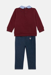 Pullover rouge bordeaux à manches longues avec un col bleu; associé à un pantalon en denim bleu foncé arborant un logo triangulaire sur le devant.