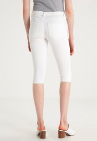 Pantalon capri en denim blanc avec un design ajusté, une longueur raccourcie et deux poches arrière, associé à des mules à talons blancs.