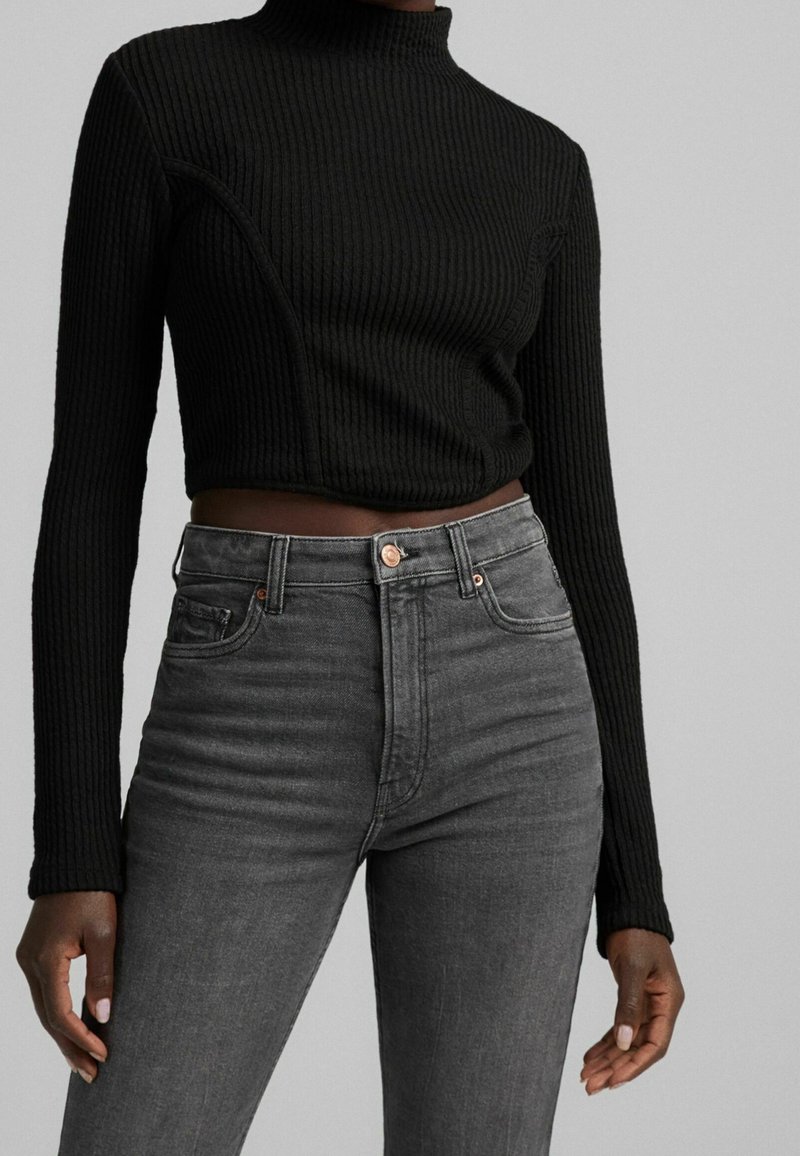 Pull à col roulé noir côtelé à manches longues, associé à un jean gris taille haute avec des détails de boutons et de poches.