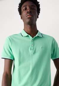 Polo de color verde menta en tejido suave, con una tapeta de dos botones, mangas cortas y cuello y puños a rayas en azul marino. Logo bordado en el pecho.