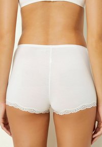 Pantaloni boyshort bianchi in cotone con un bordo in pizzo all'orlo. Il materiale appare morbido e liscio, con un design senza cuciture in vita.