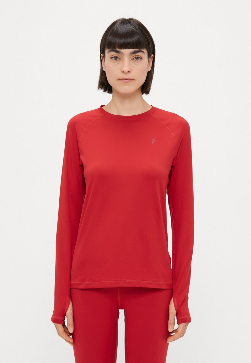 Červená, dlhá športová blúzka s raglánovými rukávmi vyrobená z hladkej, elastickej látky a s malým logom na ľavom hornom rohu.