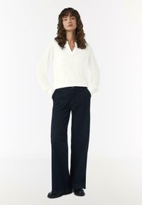Weißes Hemd mit langen Ärmeln, spitzem Kragen und gerafften Manschetten, kombiniert mit weit geschnittenen, dunkelblauen Jeans und schwarzen Ballerinas.