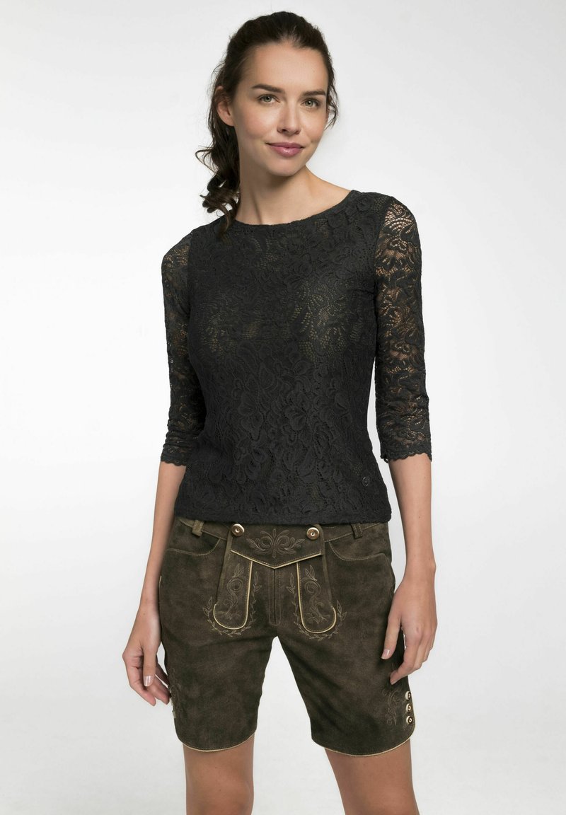 Schwarzes Spitzenoberteil mit Drei-Viertel-Ärmeln, kombiniert mit olivgrünen Wildleder-Shorts, die mit dekorativen Nähten und goldfarbener Hardware versehen sind.