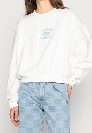 Biała bluza z okrągłym dekoltem, luźny krój, elastyczny pas i jasnoniebieski nadruk "Los Angeles 1992 California" na klatce piersiowej.