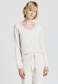 Set di abbigliamento loungewear color beige chiaro composto da una maglia a maniche lunghe con scollatura a V ondulata e pantaloni coordinati con vita elastica e cordino.