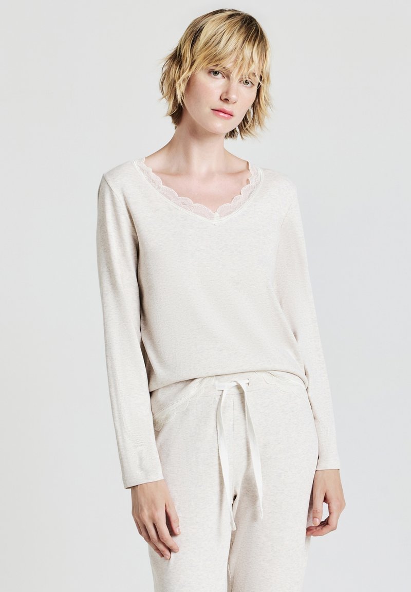 Set di abbigliamento loungewear color beige chiaro composto da una maglia a maniche lunghe con scollatura a V ondulata e pantaloni coordinati con vita elastica e cordino.
