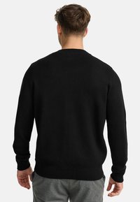 Suéter negro de punto con mangas largas, cuello redondo y puños acanalados. Textura suave con un diseño ajustado, llevado sobre pantalones grises.