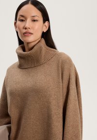 Maglione a collo alto marrone a coste in tessuto morbido, con vestibilità comoda e spalle scese. Texture liscia, dettagli di cucitura minimi.