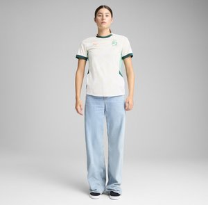 White jersey with green accents, featuring a pattern of light embossed shapes, round neckline, and short sleeves, paired with light blue wide jeans.
