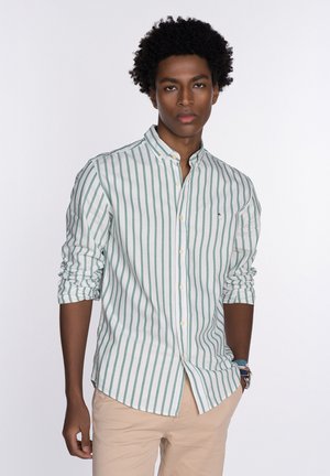Camisa de botones a rayas en verde claro y blanco. Presenta un cuello alto, mangas largas arremangadas hasta los codos y un detalle sutil del logo.