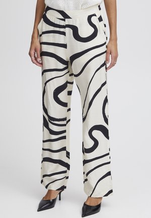Pantalons larges blancs avec des motifs abstraits noirs ondulés audacieux, fabriqués en tissu léger, associés à des talons aiguilles noirs.