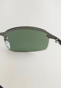 Ochelari de soare din metal cu lentile de culoare verde închis, având o formă dreptunghiulară elegantă, cu pernițe pentru nas ajustabile și un braț negru.
