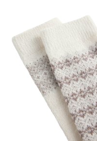 Zwei cremefarbene Wollsocken mit einem dezenten braunen geometrischen Muster nahe der Oberseite, flach auf einem weißen Hintergrund ausgelegt.