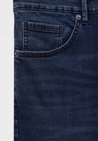 Jeans en denim bleu foncé, gros plan montrant la poche avant et la petite poche à monnaie avec des rivets métalliques sur le côté gauche.