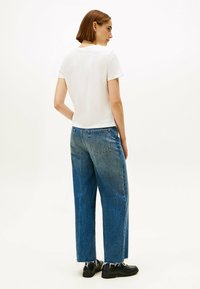 Hvid t-shirt med rund hals i kombination med løstsiddende, slidte blå jeans. Sorte sko fuldender det afslappede outfit.