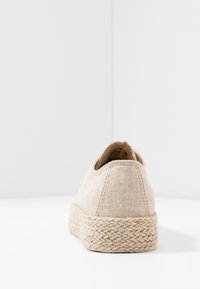 Beige canvas sko med en texturerad, vävd jute-sula. Har en rundad bakdel och minimal sömnad. Designad för avslappnad användning.