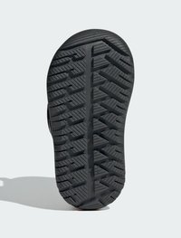 Zwarte rubberen schoenzool met een gedetailleerd loopvlakpatroon met hoekige groeven en ribbels voor grip. Rondneusontwerp.
