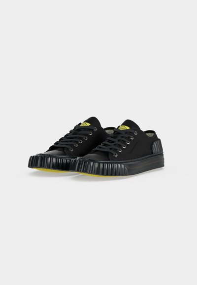 Paire de baskets basses noires avec semelles en caoutchouc côtelées et accents jaunes sur la languette et les bords de la semelle sur fond blanc.