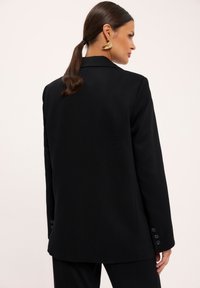 CzarnaMarynarka o dopasowanym kroju, z pojedynczym rozcięciem z tyłu, mankietami na trzy guziki oraz gładkim, strukturalnym materiałem. Minimalistyczny design.