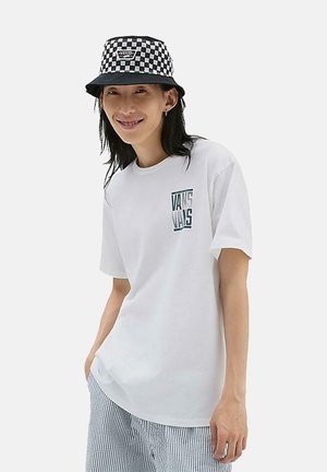 Camiseta blanca de algodón de manga corta con un pequeño gráfico de 'Vans' en teal en el pecho. Combinada con pantalones a rayas y un sombrero de cubo a cuadros.