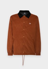 Brown corduroy jacket with a black collar, snap button closure, adjustable drawstring hem, and side pockets; features logo on the chest.