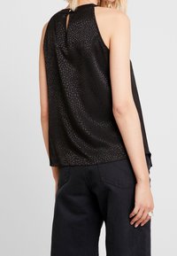 Svart linne med ett texturerat mönster, ryggdesign med nyckelhål och lös passform. Matchat med mörka byxor, som visar en avslappnad stil.