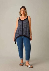 Svart och vit mönstrad linne med V-ringning, ihop med blå denimjeans och silverfärgade slidesandaler med en rosettdetalj.