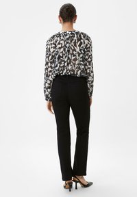 Zwarte slim-fit broek gecombineerd met een transparante blouse met abstracte witte en blauwe patronen. De silhouette is gestroomlijnd, met minimale hardware.