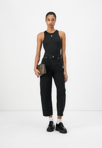 Černý bodysuit, černé džíny s vysokým pasem, černé robustní boty a malá šedá kabelka. Hladký materiál, přiléhavý střih, decentní logo detail.