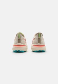 Lightweight running shoes with a textured beige upper, pink accents, green heel tab, and a thick cream midsole with turquoise outsole.