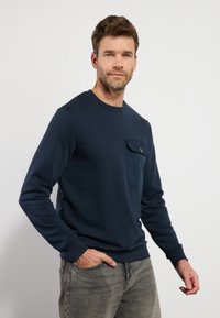 Navyblauwe sweatshirt van een katoenmix, met een voorzak met een knop, ronde halslijn en lange mouwen. Draag het met grijze jeans.
