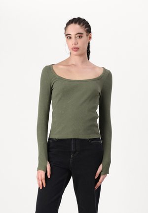 Haut en ribbed à manches longues de couleur vert olive avec un décolleté large et une silhouette ajustée, associé à un jean foncé pour le contraste.
