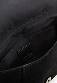 Vnitřek černé látkové kabelky se zobrazenou kapsou a prošitým černým koženým štítkem s embosovaným nápisem "SEA&JODD".