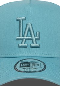 Boné de beisebol azul-claro com um logótipo "LA" bordado. Apresenta uma fivela ajustável e uma etiqueta circular marcada como "New Era Adjustable."