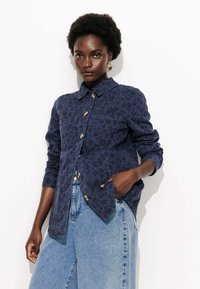 Chemise boutonnée bleu marine avec imprimé léopard, deux poches poitrine et col étalé. Réalisée en tissu texturé avec des manches longues.