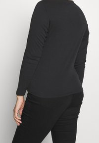 Schwarzes Langarmshirt mit taillierter Passform, runden Ausschnitt und glatter Textur, kombiniert mit schwarzen, engen Jeans mit einer Rückentasche.