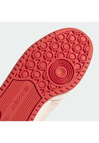 Suola di sneaker rossa in gomma con motivo di trazione circolare e marchio impresso. Aree testurizzate evesse per il dettaglio della presa.