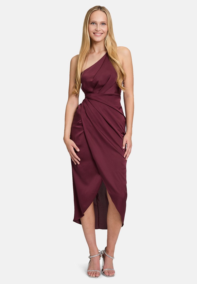 Robe bordeaux à une épaule avec un tissu drapé, longueur mi-mollet, dotée d'une fente sur le côté et d'une texture lisse. Associée à des sandales à talons argentées.